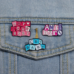 Three colorful enamel pins with Cry Baby text on denim jacket pocket closeup