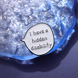 White speech bubble enamel pin with 'I have a hidden disability' text on blue display