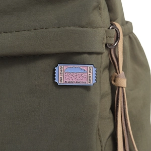 Close-up of enamel pin with cloud pattern and ALWAYS ANXIOUS text on green canvas bag