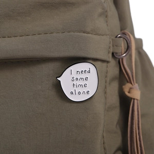 White speech bubble enamel pin with I need some time alone text on green canvas bag