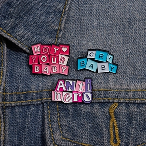 Detailed view of three enamel letter pins featuring slogan text on a denim jacket.