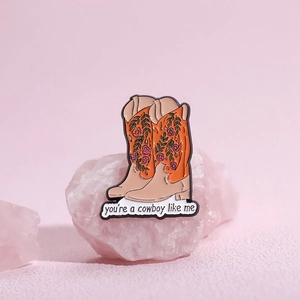 Orange cowboy boot enamel pin with floral details and cowboy like me banner text