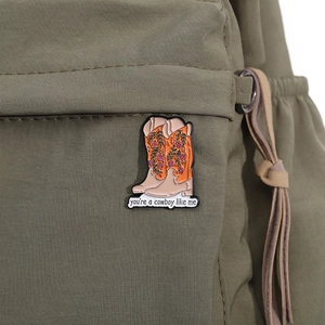 Detail of cowboy boot enamel pin with floral pattern on olive green canvas bag