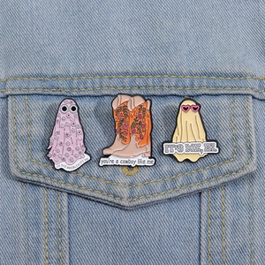 Three creative enamel pins on denim jacket showing ghost and cowboy boot designs