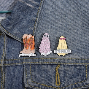 Detailed close-up of ghost and floral cowboy boot enamel pins on blue denim fabric