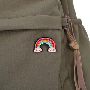 Detailed macro view of a colorful rainbow enamel pin with smiling pink clouds on green canvas
