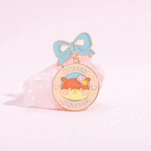 Cartoon-Otter-Emaille-Pin mit blauer Schleife und 'Otterly Adorable' Text auf Rosa Hintergrund