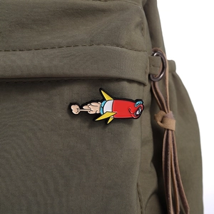 Detail of red cartoon rocket enamel pin attached to a green canvas bag background