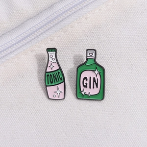 Vista dettagliata delle spille smaltate GIN e TONIC su tessuto di tela bianca