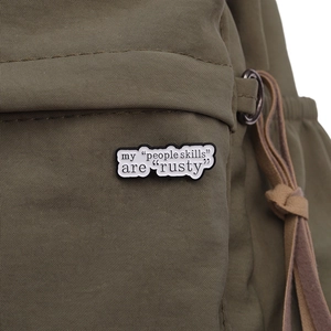 Close-up of speech bubble lapel pin with my people skills are rusty text on green fabric