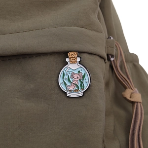 Detailed close-up of a pink axolotl enamel pin in a glass bottle on a green canvas backpack