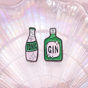 Spille smaltate con bottiglie di tonic rosa e gin verde su vassoio di perle