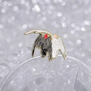 Creative black and white enamel wing pin with gold metal finish on glass background