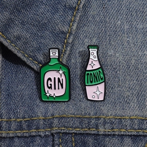 Dettaglio delle spille smaltate GIN e TONIC appuntate su una giacca di jeans blu