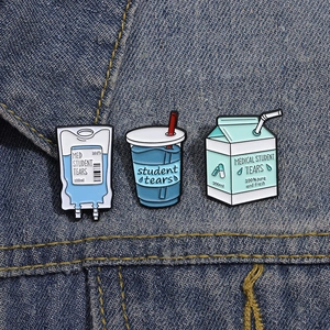 Funny Student Tears enamel pin set with blue milk carton and IV bag on denim jacket