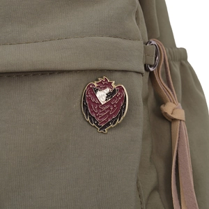 Detailed enamel pin with red-winged angel embrace pinned on a green nylon backpack