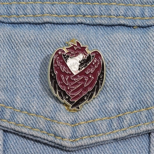 Detail of red winged angel and demon heart enamel pin on a denim jacket pocket