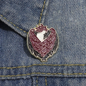 Anime enamel pin with heart-shaped wings on blue denim background for backpacks