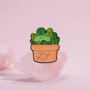 Cute enamel pin featuring a cartoon frog in a green potted plant with orange terracotta pot