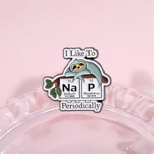 Cartoon sloth enamel pin with chemical elements Na and P forming the word NAP on glass