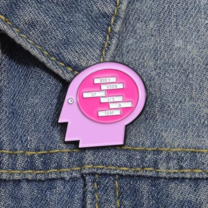 Pink face silhouette enamel pin with Don't Grow Up It's A Trap text on denim fabric