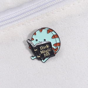 Creative cartoon enamel pin featuring a mint green character reading a Dark Magic book