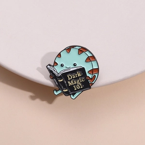 Macro detail of cartoon enamel pin featuring a mint monster reading Dark Magic 101 book