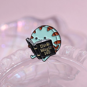 Cute mint green cookie enamel pin reading a Dark Magic 101 book on an iridescent tray