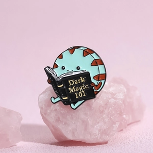 Cartoon enamel pin featuring a round blue character reading a Dark Magic 101 book