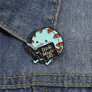 Cartoon enamel pin of a blue character reading a Dark Magic book on denim jacket