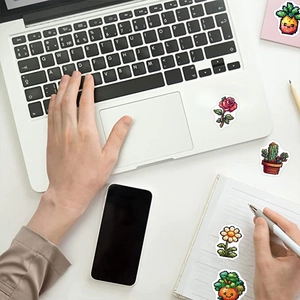 Macro view of pixel art stickers on laptop and notebook featuring flowers and cactus