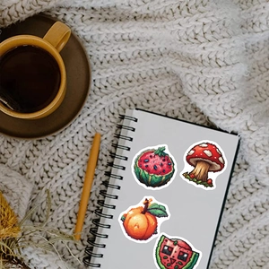 Close-up of pixel art fruit stickers on a notebook page in a cozy home setting