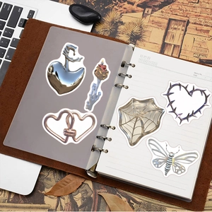 Detailed view of silver metallic 3D stickers with skull and heart motifs on a vintage notebook