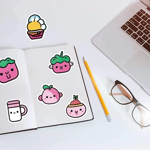 Nahaufnahme süßer Frucht-Sticker auf einem Notizbuch mit Büro-Accessoires am Tisch