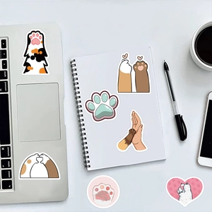 Detail of cute cat paw stickers applied on a silver laptop and white notebook