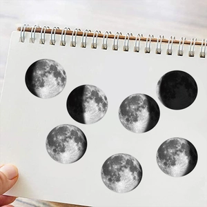 Detail of seven minimalist black and white moon phase stickers on a white notebook page