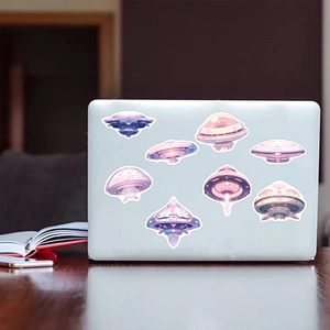 Close-up of colorful UFO cartoon stickers applied on a silver laptop with aesthetic desk setup