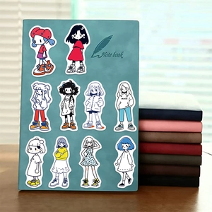 Detail of 10 hand-drawn cartoon girl stickers arranged on a green notebook cover