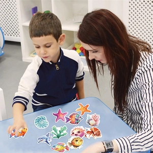 Kid and parent playing with colorful cartoon sea creature stickers on a blue table