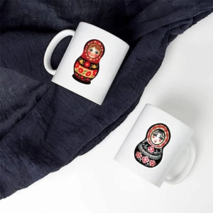 Detail of two white ceramic mugs featuring red and black Matryoshka doll floral patterns