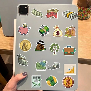 Cartoon money stickers applied on a grey tablet held by a hand over a wooden desk