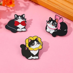Detailed view of three cute black and white enamel cat pins on a soft pink background