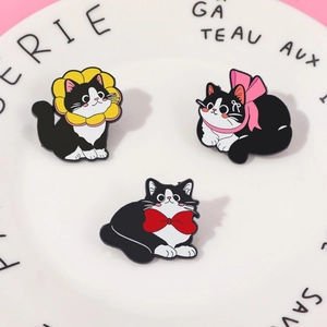 Detailed view of three cute black and white cat enamel pins with colorful bows on a tray