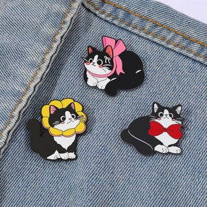 Three cute cartoon black and white cat enamel pins pinned on blue denim fabric