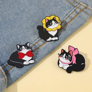 Detailed view of three cute black and white cartoon cat enamel pins on blue denim fabric