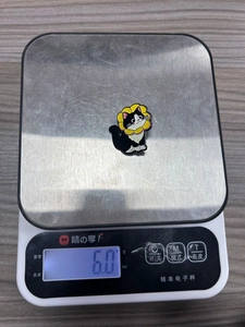 Detail shot showing the 6.0g weight of the black and white cat enamel pin on a scale