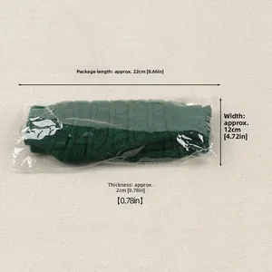 Macro detail of dark green chunky knit wool gloves in clear protective packaging