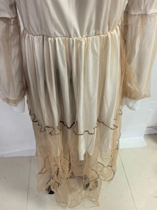 Détails de la robe en tulle beige avec manches bouffantes et finitions de couture ondulées