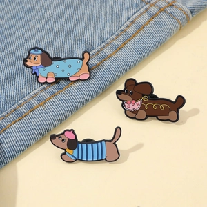 Vue détaillée de trois épinglettes en émail teckel de dessin animé sur denim et beige