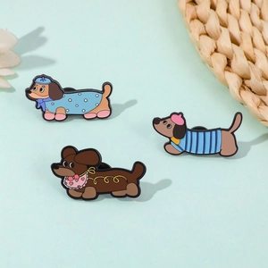 Détail de trois épingles en émail de teckel de dessin animé avec des tenues colorées